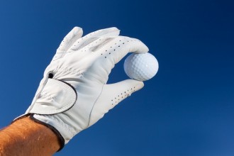 Hand wearing golf glove holding a white golf ball over a deep blue sky.