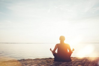 Young woman doing meditation practice on the beach. Intentional sun glare and lens flare effect