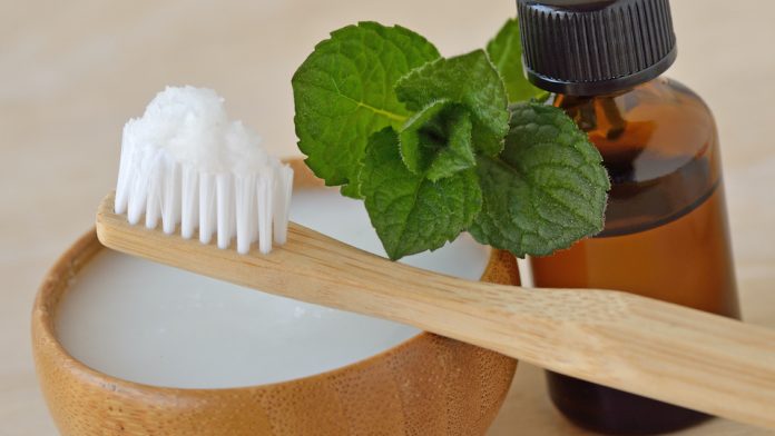 Coconut oil in a bowl with a wooden toothbrush and peppermint essential oil - Homemade natural toothpaste