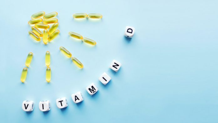 Yellow capsules in the form of the sun with rays and the word vitamin D from white cubes with letters on a blue background. VITAMIN D word for healthy and medical concept. Sunshine vitamin health benefits
