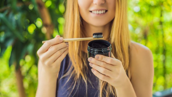 Young woman brush teeth using Activated charcoal powder for brushing and whitening teeth. Bamboo eco brush